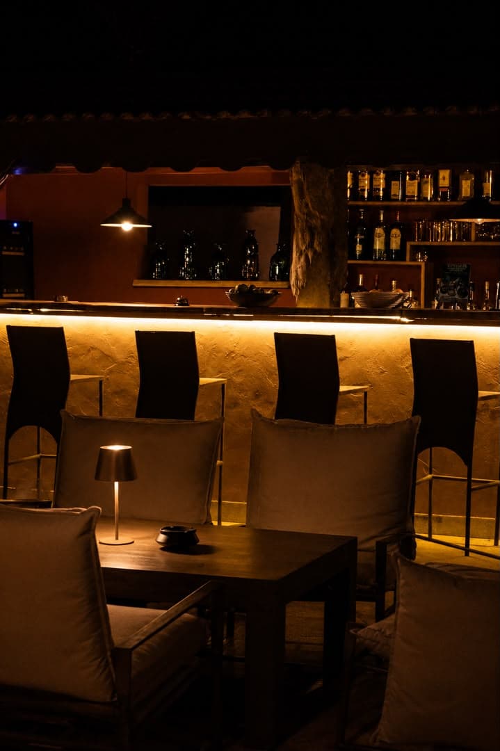 Le bar de Gorée Suites la nuit : comptoir éclairé, bouteilles et tabourets hauts