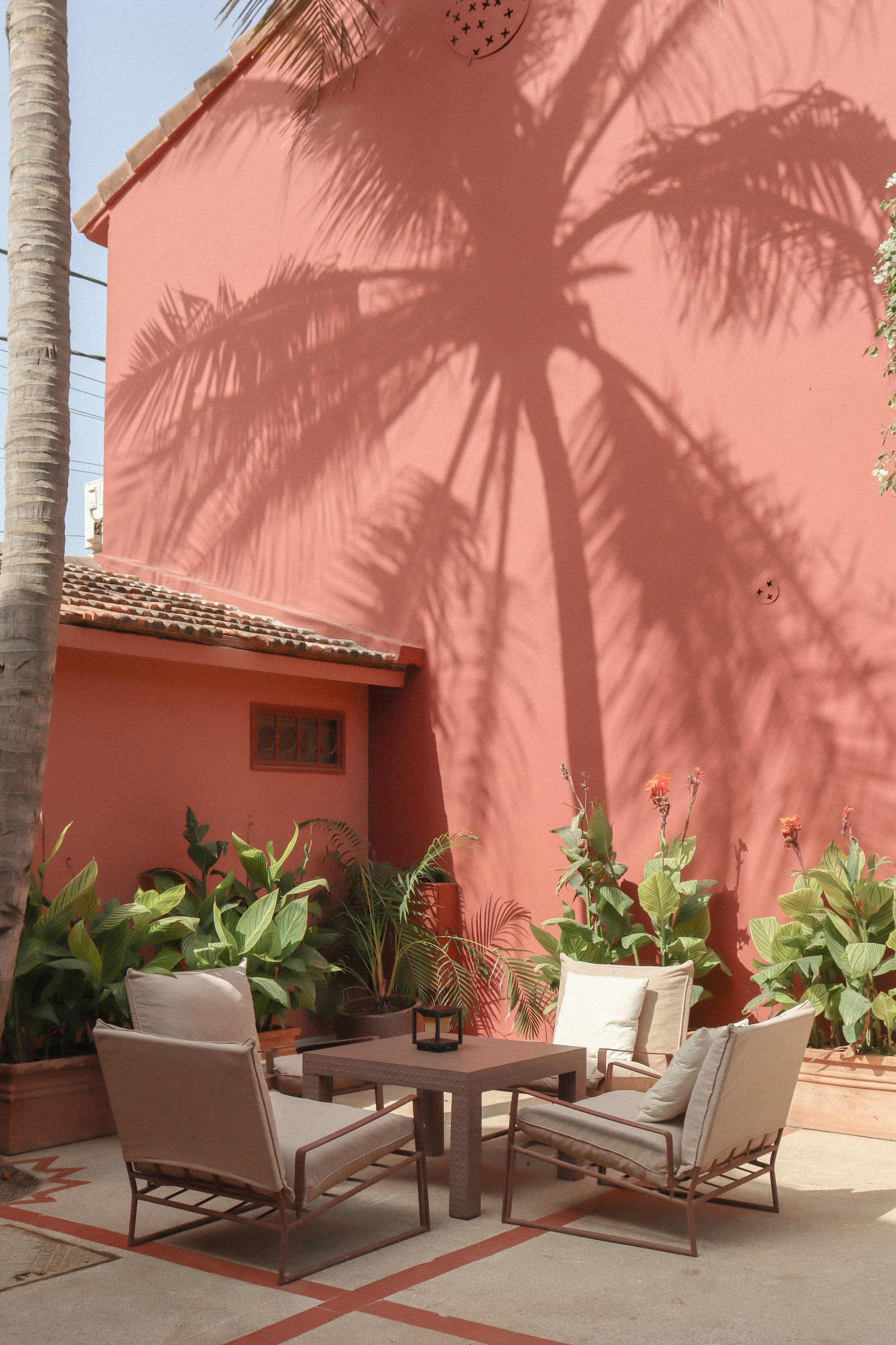 Patio de Gorée Suites, ombre des palmiers sur le mur ocre et salon de jardin