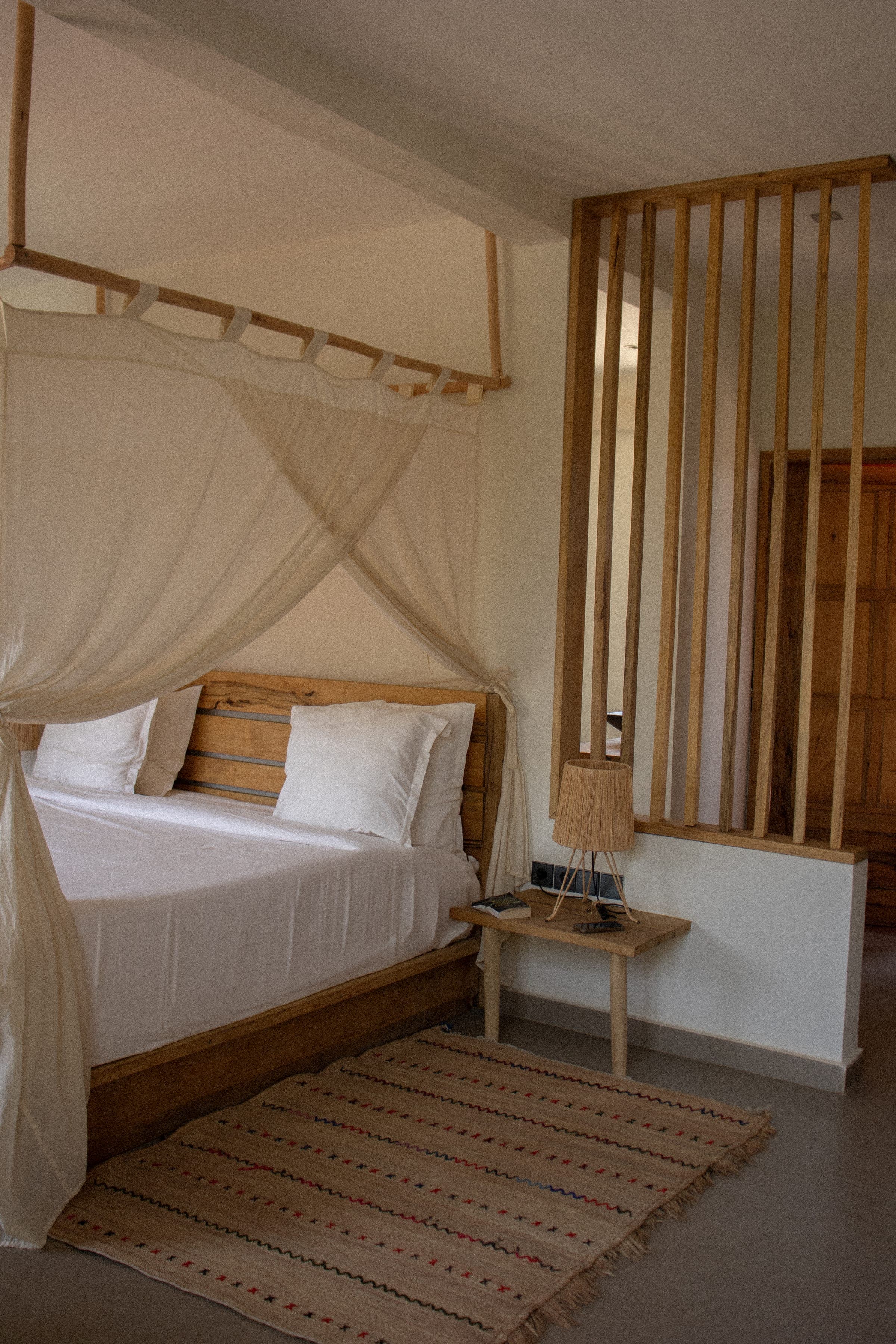 Chambre de Gorée Suites avec lit à baldaquin en bois clair et voilage